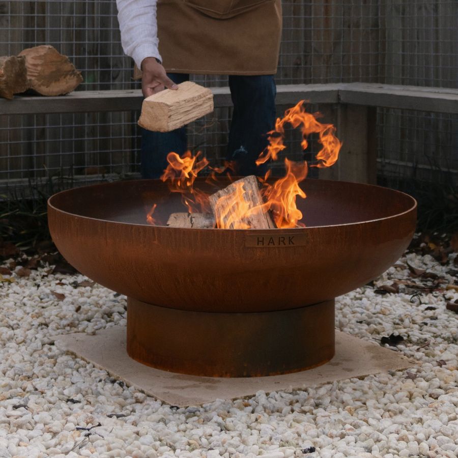 Person in an apron lighting a fire in a metal fire pit outdoors.